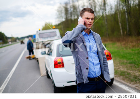 Man calling while tow truck picking up his broken 29507831