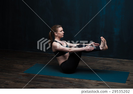 Fit girl practicing yoga asana against dark wall Fit girl practicing yoga asana against dark wall 29535202