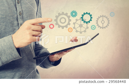 Young man pointing at gears over a tablet computer Young man pointing at gears over a tablet computer 29568448