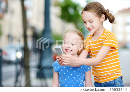 Two cute little sisters playing outdoor mobile game on their smart phones 29633244