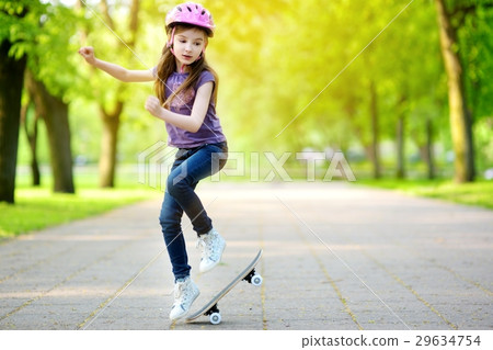 Pretty little girl learning to skateboard outdoors 29634754