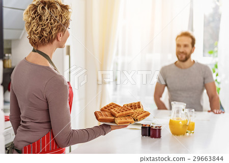 Cheerful housewife serving waffles on table Cheerful housewife serving waffles on table 29663844