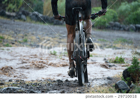 Mountain biker driving in rain upstream creek Mountain biker driving in rain upstream creek 29710018