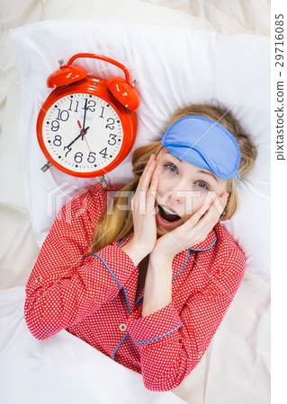 Shocked woman wearing pajamas holding clock overslept Shocked woman wearing pajamas holding clock overslept 29716085