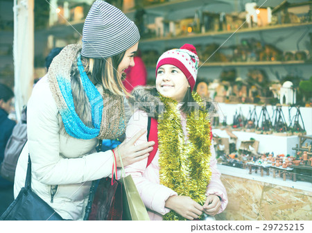 Female customers staring at counter of kiosk with figures for creating miniature Christmas scenes 29725215