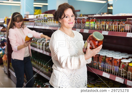 Cheerful female customers looking at jars with pickles Cheerful female customers looking at jars with pickles 29725278