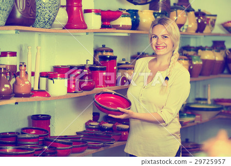 Portrait of glad woman choosing glazed with red color ceramic utensil Portrait of glad woman choosing glazed with red color ceramic utensil 29725957