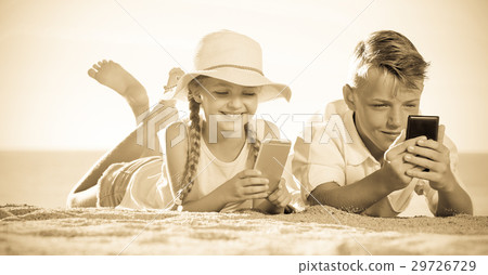 Smiling kids on beach with phone in hands Smiling kids on beach with phone in hands 29726729