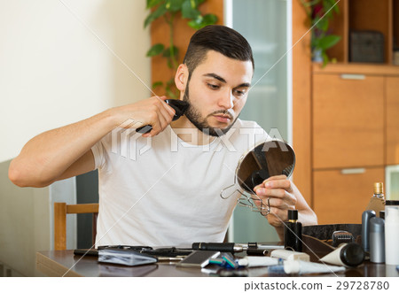 guy looking at mirror and shaving beard with trimmer guy looking at mirror and shaving beard with trimmer 29728780