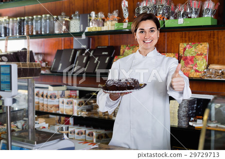 Woman seller showing warm festive chocolate cake Woman seller showing warm festive chocolate cake 29729713