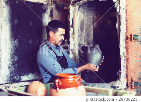 satisfied male with black-glazed ceramic vase standing close to kiln satisfied male with black-glazed ceramic vase standing close to kiln 29730223