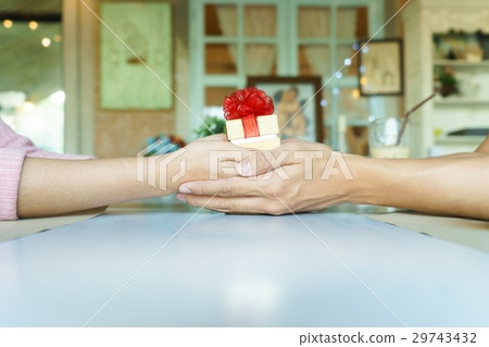 A couple hands holding a gift box with red ribbon A couple hands holding a gift box with red ribbon 29743432