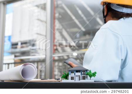 House architectural model and workers supervising the workers watching the tablet at the office 29748201
