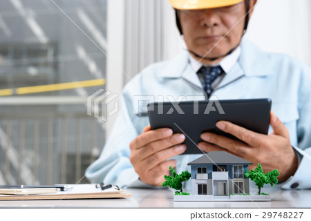 House architectural model and workers supervising the workers watching the tablet at the office 29748227
