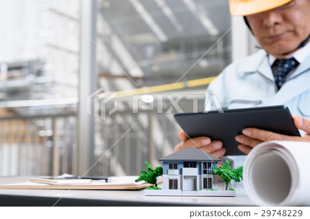 House architectural model and workers supervising the workers watching the tablet at the office 29748229