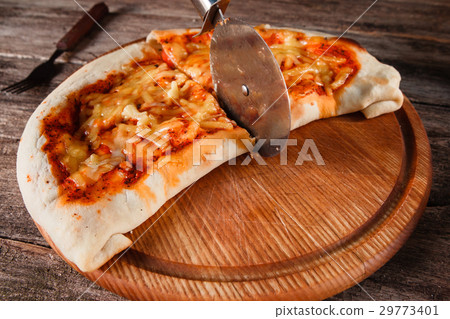 Pizza calzone cut with wheel on wooden platter 29773401