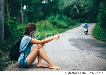 Young beautiful woman hitchhiking sitting on road Young beautiful woman hitchhiking sitting on road 29779744
