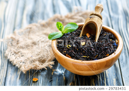 Bowl of black tea and a wooden scoop. 29783431
