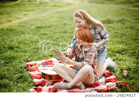 图库照片: two girls looking in the tablet at the picnic