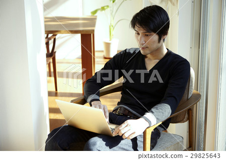 坐在一把椅子在一個晴朗的屋子和使用計算機的一個人 坐在一把椅子在一個晴朗的屋子和使用計算機的一個人 29825643