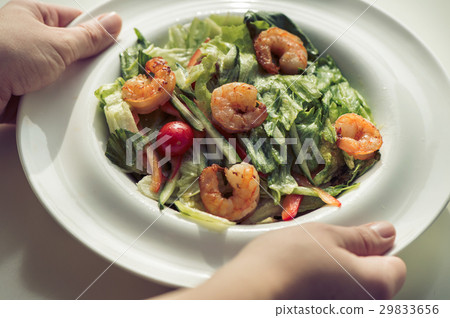 Female hands hold a plate with shrimp salad.  29833656