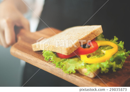 Woman holding sandwich on wooden pan. 29835873