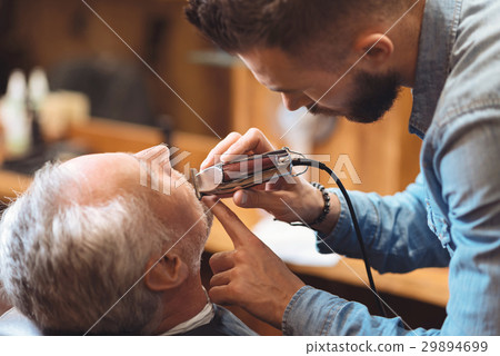 Charismatic barber shaping beard of the client in 29894699