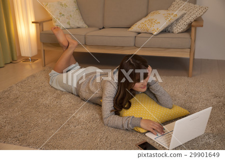 A woman surfing the net while lying on the floor 29901649