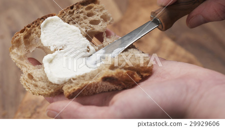 spreading ricotta cheese on fresh rustic bread 29929606