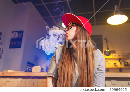 Young pretty woman in red cap smoke an electronic Young pretty woman in red cap smoke an electronic 29964025