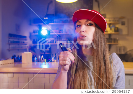Young pretty woman in red cap smoke an electronic Young pretty woman in red cap smoke an electronic 29964127