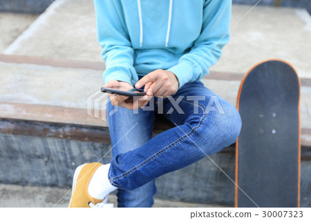 young skateboarder use cellphone  at skatepark 30007323