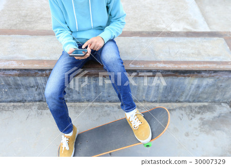 young skateboarder use cellphone  at skatepark 30007329