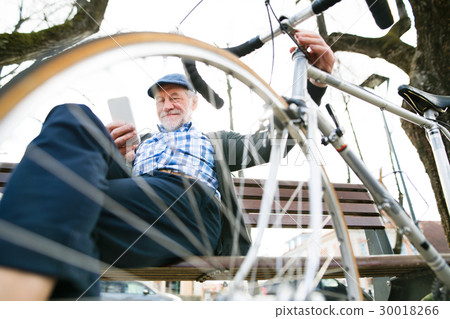 Senior man with bicycle in town, holding smart 30018266