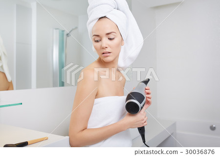 Young woman blow drying hair in bathroom Young woman blow drying hair in bathroom 30036876