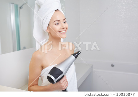 Young woman blow drying hair in bathroom Young woman blow drying hair in bathroom 30036877