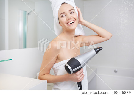 Young woman blow drying hair in bathroom Young woman blow drying hair in bathroom 30036879