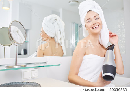 Young woman blow drying hair in bathroom Young woman blow drying hair in bathroom 30036883