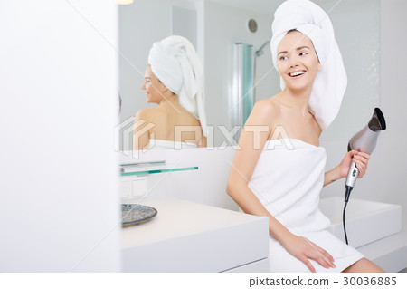 Young woman blow drying hair in bathroom Young woman blow drying hair in bathroom 30036885