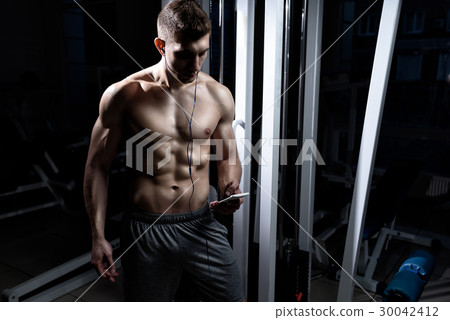 Man listening to music on headphones in the gym 30042412