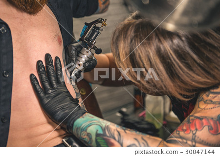 Woman creating tattoo on body of client Woman creating tattoo on body of client 30047144