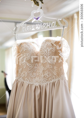 Beige wedding dress hangs on white peg with 30068806