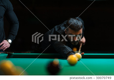 Young man playing billiard in dark club. 30070749