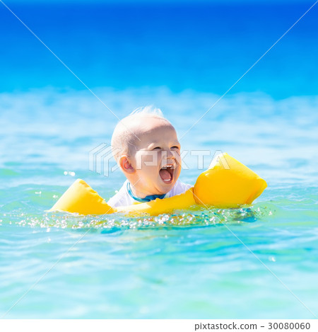 Baby swimming in ocean water on tropical beach 30080060