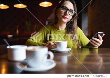 Young woman drinking coffee and using smartphone in cafe Young woman drinking coffee and using smartphone in cafe 30089622