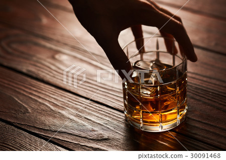 Glass of whiskey with ice cubes on wooden table 30091468