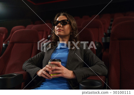 Young woman watches movie 3D at the cinema and drinks coffee, lo Young woman watches movie 3D at the cinema and drinks coffee, lo 30100111