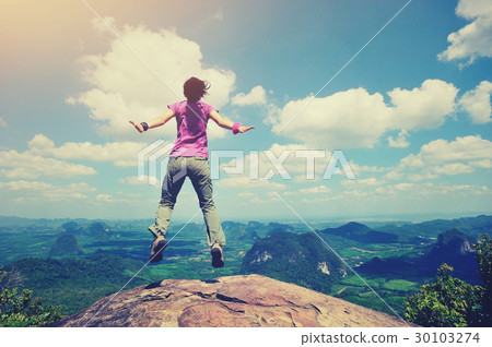 cheering oung woman jumping on mountain peak 30103274