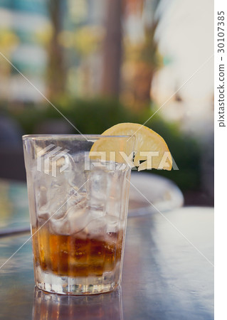 Glass with cola, ice and lemon on a table outside 30107385