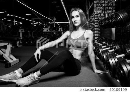 Young slim girl sitting next to dumbbells in gym 30109199